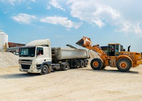 Excavator loading materials into a heavy-duty truck at a sunny construction site.