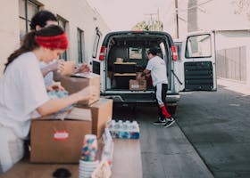 Volunteers organize and load boxes of donated supplies into a van for distribution.