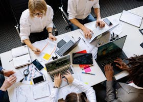 Vibrant office teamwork scene with laptops, documents, and diverse professionals in a meeting.