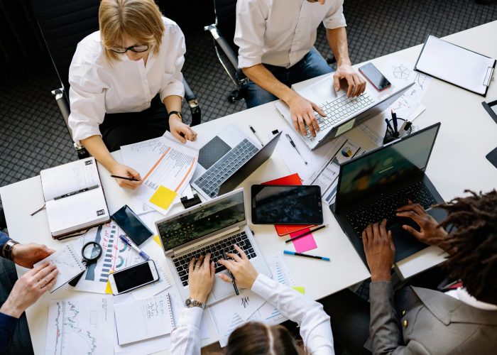 Vibrant office teamwork scene with laptops, documents, and diverse professionals in a meeting.